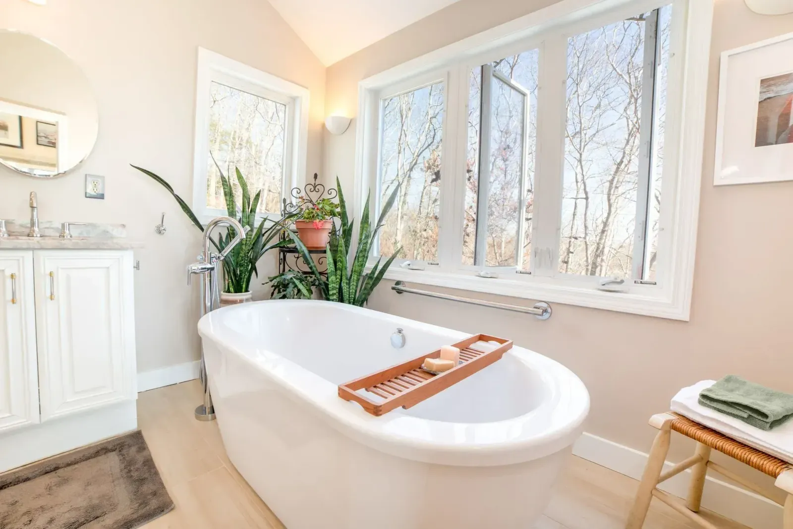 Bright bathroom with a white clawfoot tub, large windows, plants, and a small wooden stool
