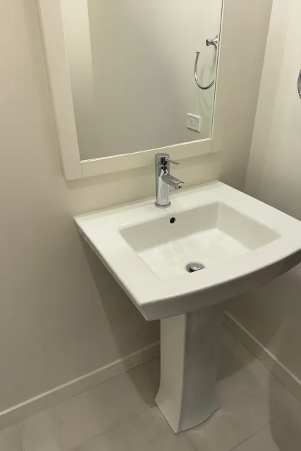 White pedestal sink in a bathroom with a chrome faucet and mirror.