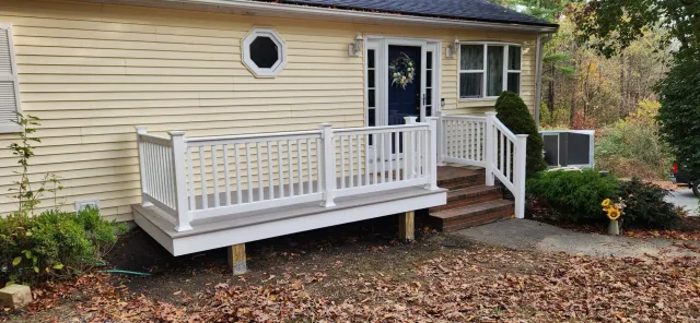 Front porch with white railing and steps leading to a blue door on a yellow house. Autumn leaves scattered on the ground.