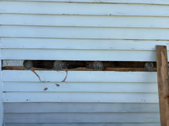 Broken wooden fence rail against white siding with hanging wires
