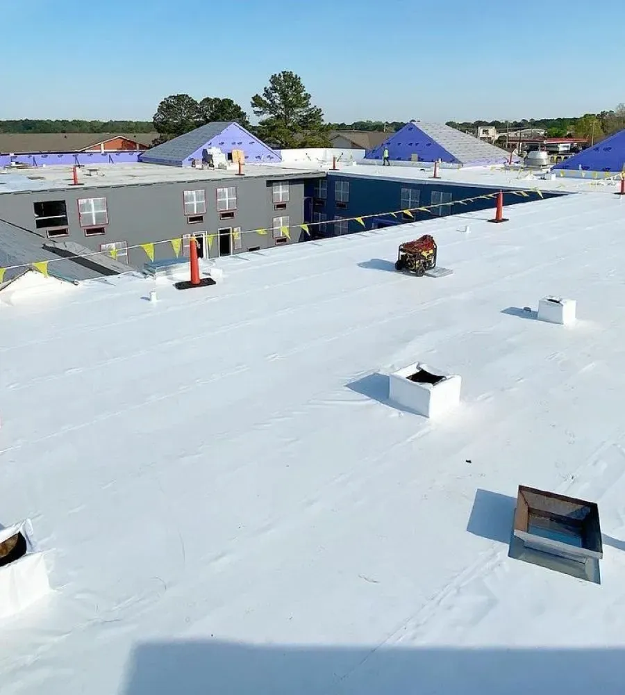 White rooftop with vents and skylights overlooking nearby buildings under a blue sky.