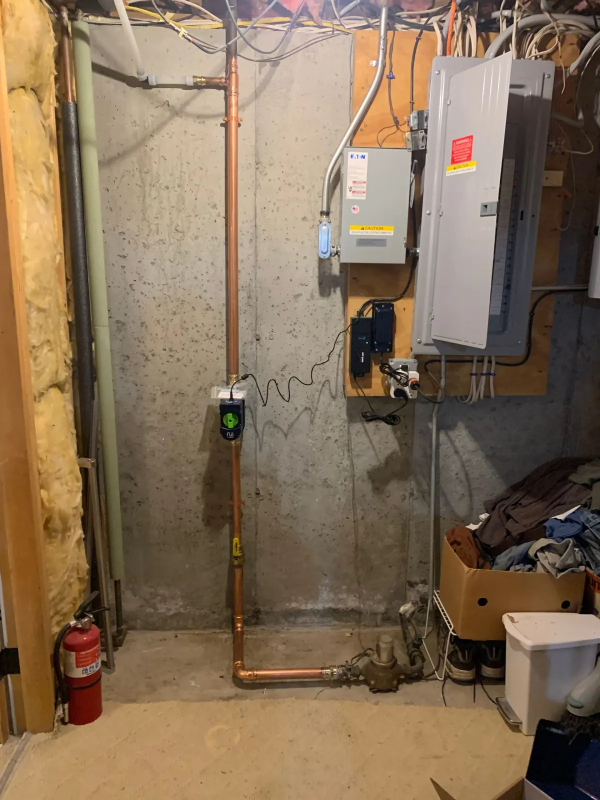 Basement with copper pipes, electrical panel, and fire extinguisher against a concrete wall.