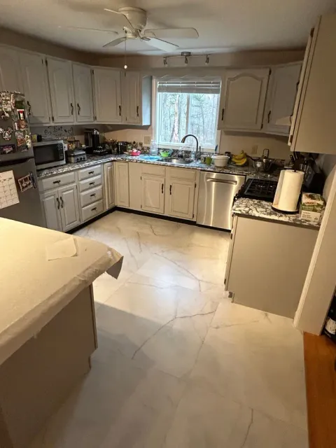 Bright kitchen with white cabinets, tiled floor, and a window above the sink cluttered with dishes.