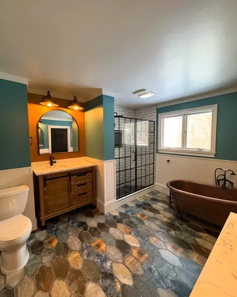 Modern bathroom with teal walls, mosaic tile floor, vanity, shower, and a freestanding tub by the window