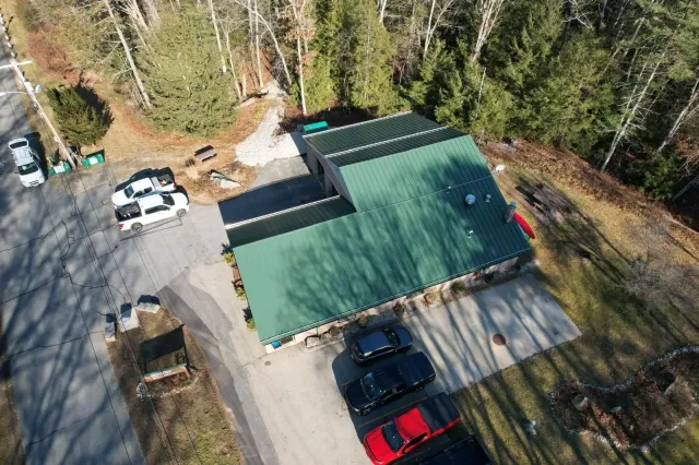 Aerial view of a green-roofed building surrounded by trees and parked vehicles on a driveway.