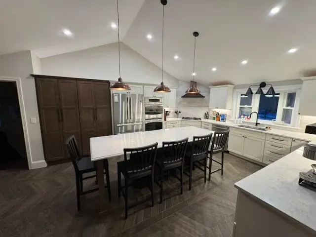 Modern kitchen with white cabinets, stainless steel appliances, a large island with barstools, and black pendant lights overhead.