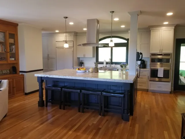 Modern kitchen with an island, beige cabinets, stainless steel appliances, hardwood floors, and a large window above the sink.