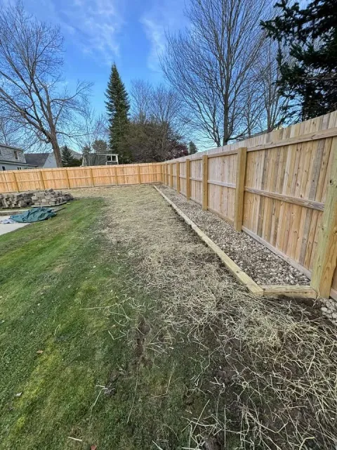 A backyard with a newly installed wooden fence, new drainage, straw put down for new grass