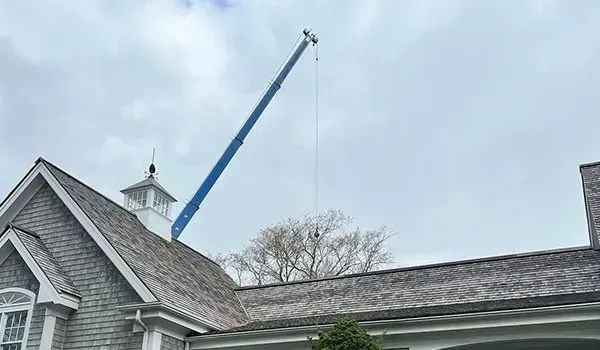 Blue crane lifting a roof section on a house under cloudy sky