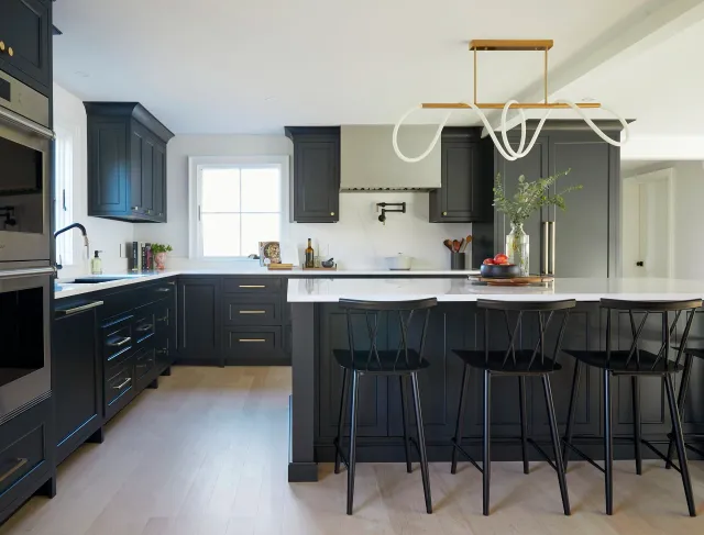 Modern kitchen with black cabinetry, white countertops, black stools at an island, a window, and decorative lighting fixture.