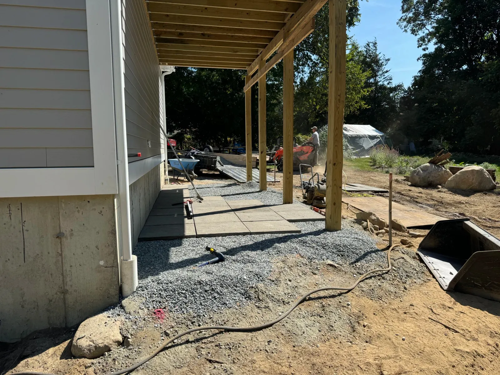 Backyard construction scene with wooden beams, concrete foundation, and gravel pathway