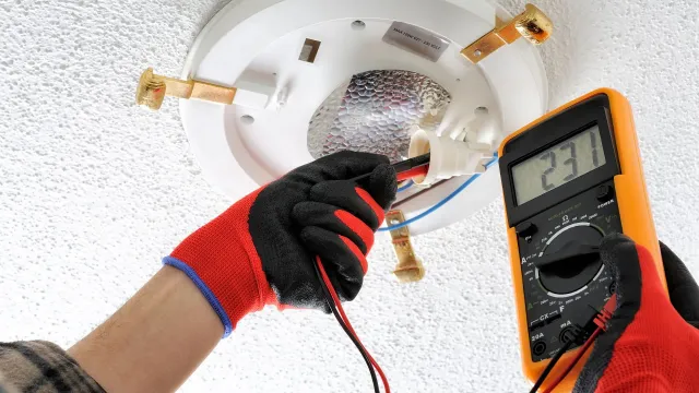 A person is using a multimeter to test a smoke detector.