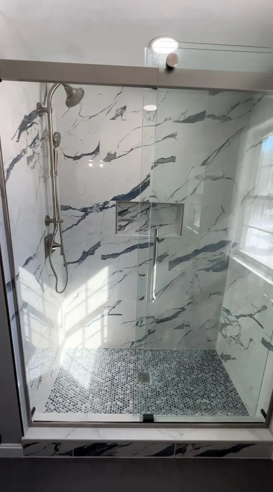 Marble-tiled shower stall with a pebble floor and glass enclosure.
