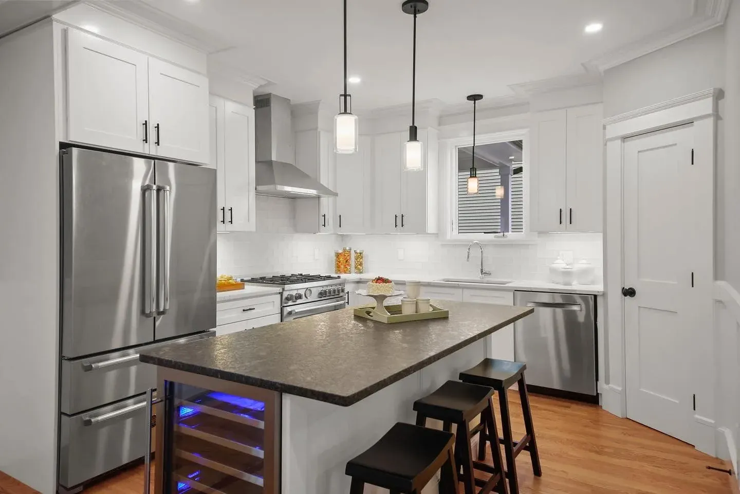 Kitchen with white cabinetry, a stone-top island with seating and a fitted wine cabinet