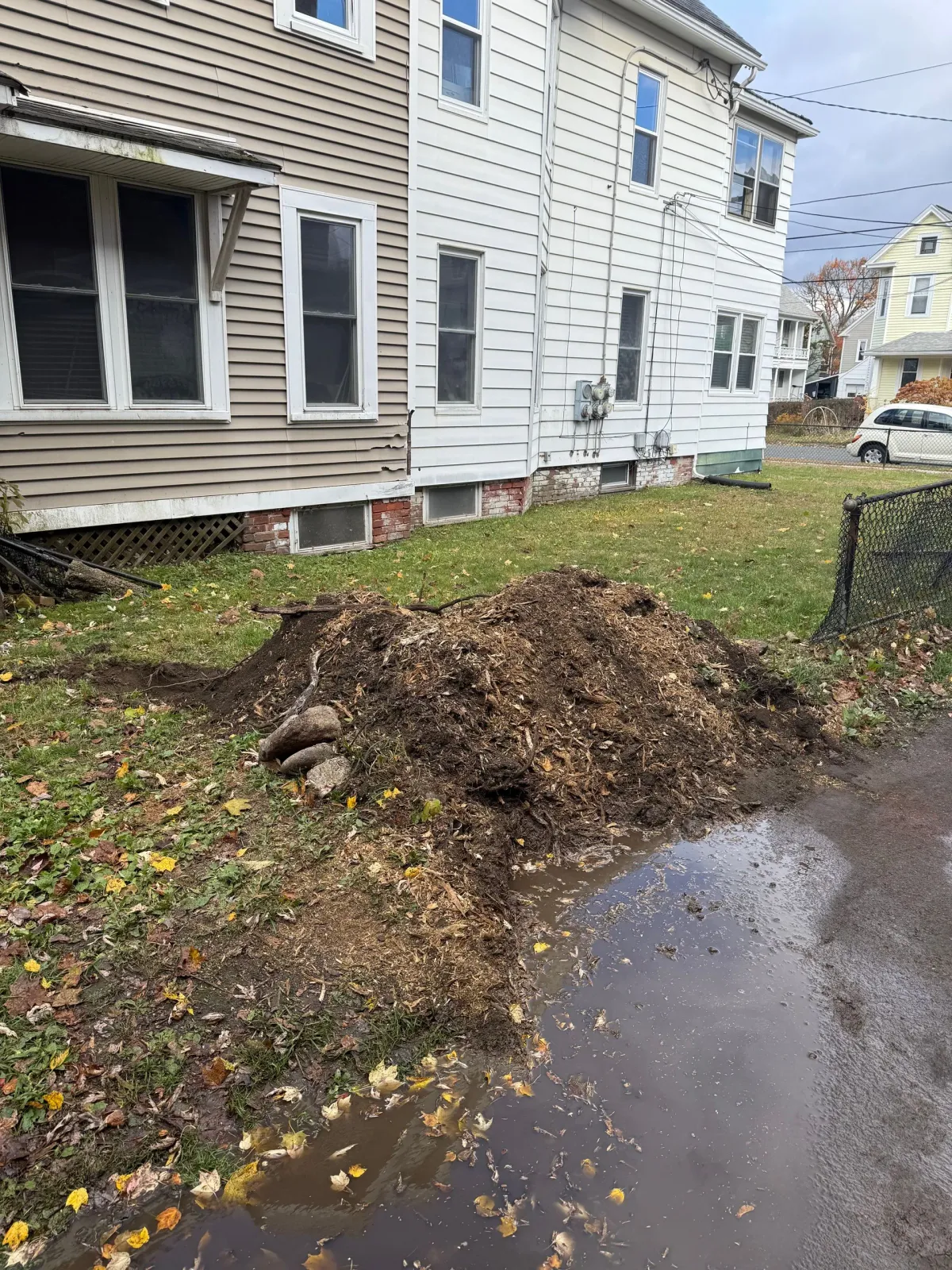 Pile of mulch and leaves on a lawn next to a two-story house with gray siding.