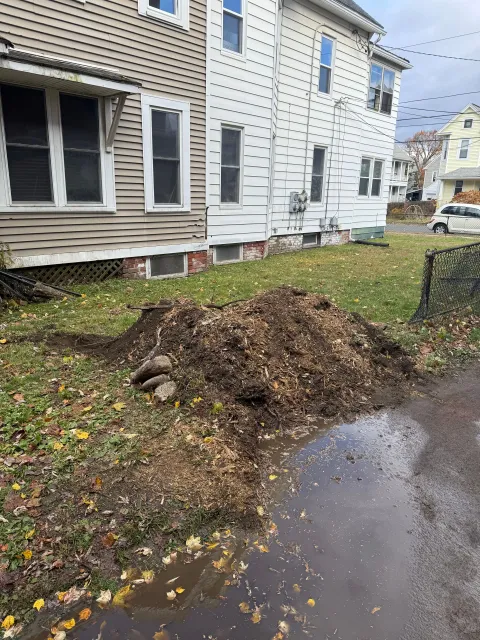 Pile of mulch and leaves on a lawn next to a two-story house with gray siding.