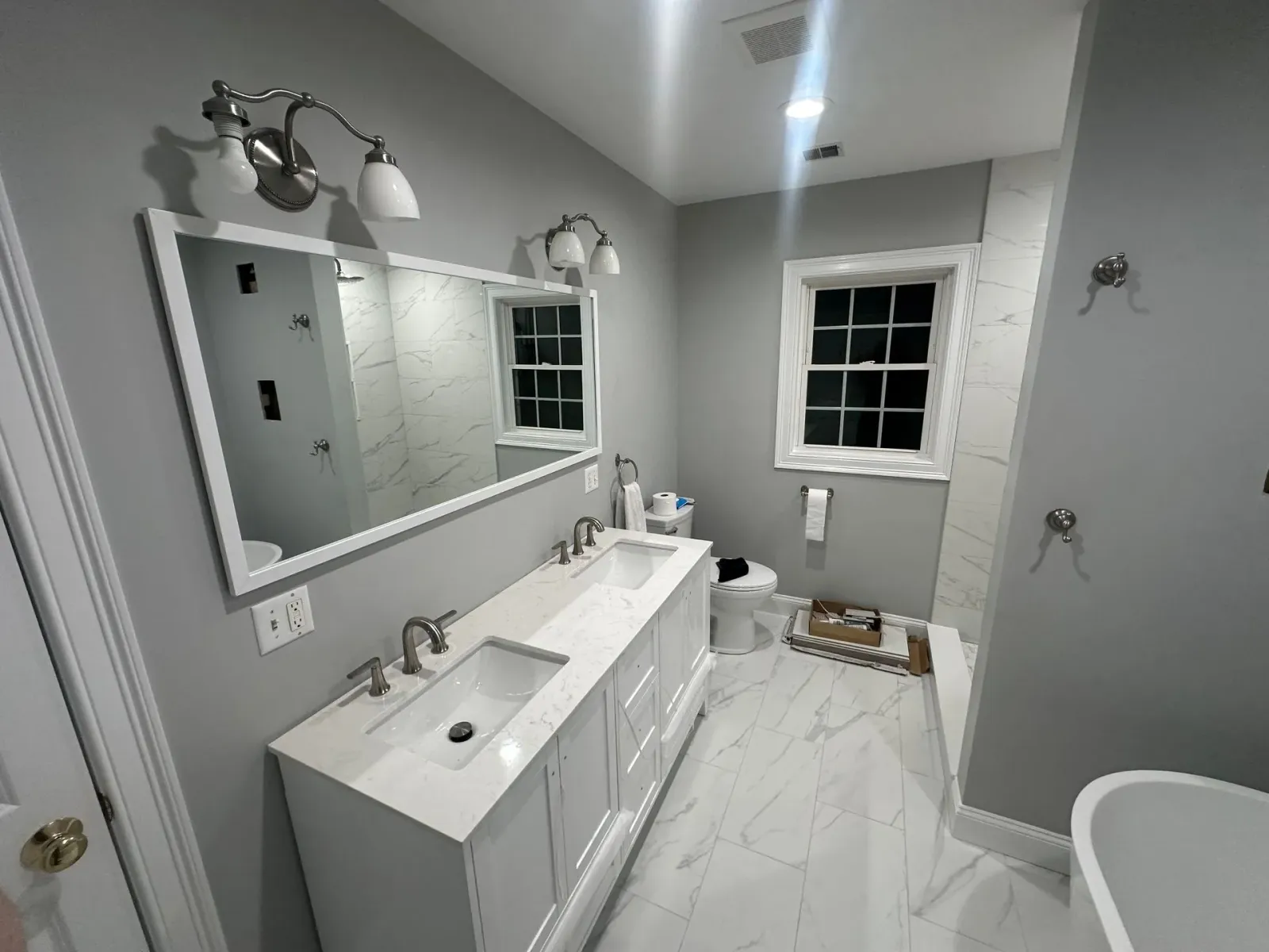 Bathroom with a white vanity, marble floor, and gray walls, featuring a large mirror and window.