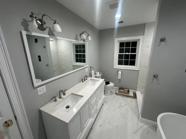 Bathroom with a white vanity, marble floor, and gray walls, featuring a large mirror and window.