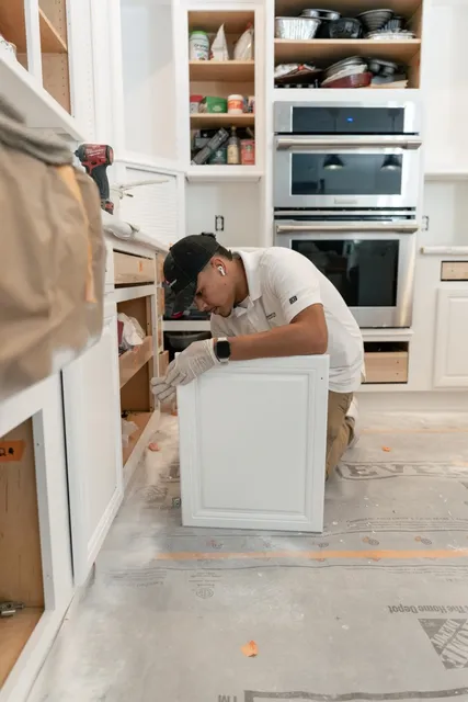 Pedretti's Cabinet Co. team member kneeling while reinstalling a painted cabinet door