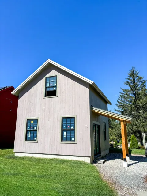 New two-story house with beige siding, four windows, a sliding glass door, and a small porch under construction, set on a grassy lawn under a clear blue sky.