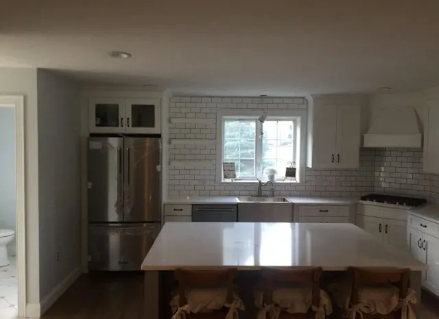Spacious kitchen with island, stainless steel appliances, white cabinetry, and a brick backsplash.