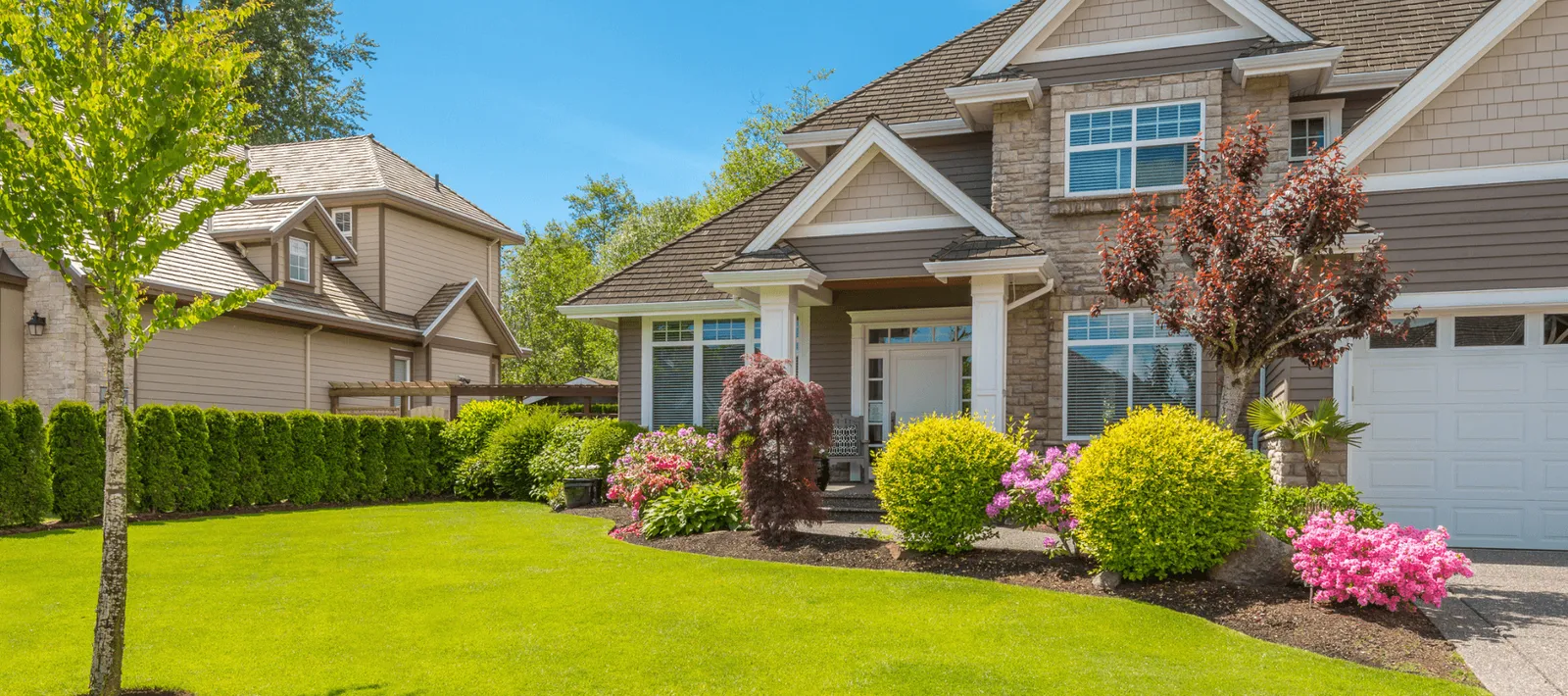 Bright green manicured lawn with shaped shrubs, flowering azaleas and clean mulch beds in front of a South Coast Massachusetts home