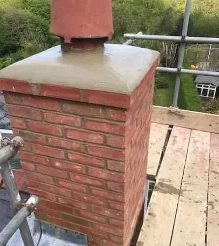 A red brick chimney stack on a residential roof, featuring a newly applied concrete crown and a terracotta chimney pot.