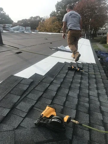 Roofer works on a roof with visible shingles, nails, and protective layer.