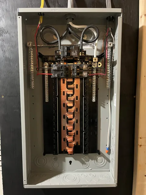 Open electrical breaker panel with multiple circuit breakers and wiring inside a gray metal box.