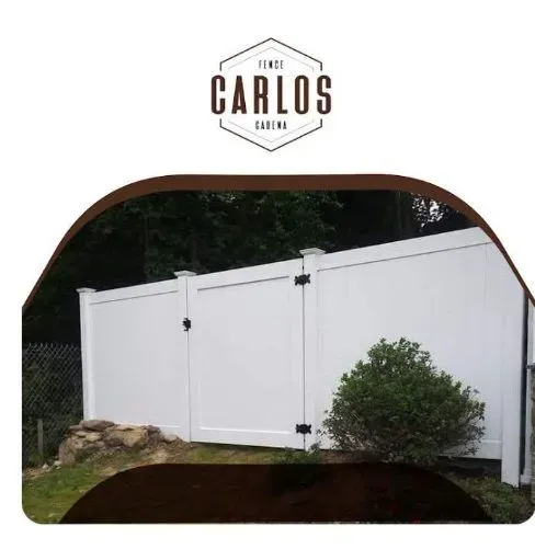 White vinyl fence with gate in front of trees.