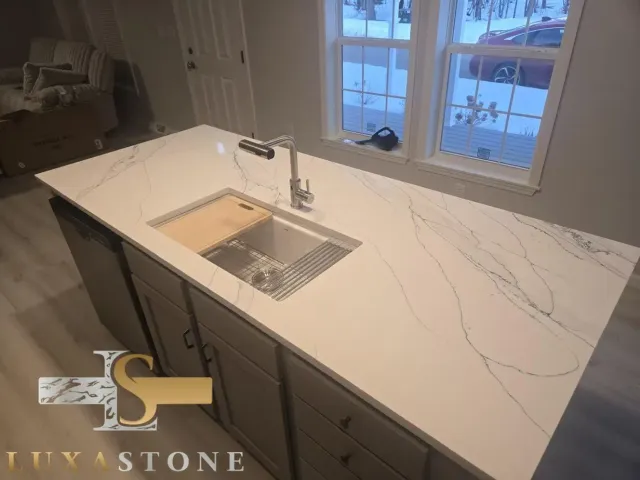 Modern kitchen island with white countertop and built-in sink, gray cabinets, and window.