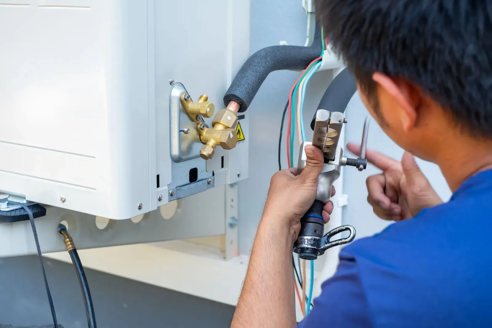 Technician adjusting wiring and connections on an outdoor HVAC unit