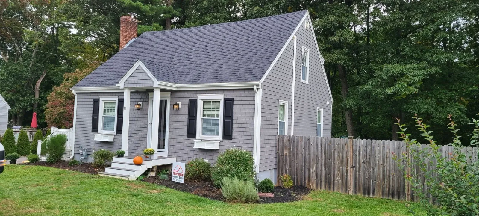 Gray house with a dark roof and a picket fence in front of greenery.