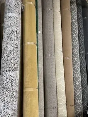 Rolled-up carpet samples in various colors and patterns displayed side by side; beige, gray, patterned, and solid.