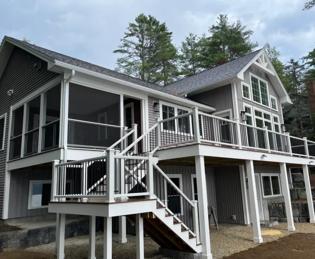 Multi-story house with gray and white exterior, large windows, and multiple decks with railings, surrounded by trees.