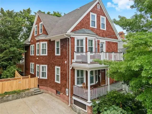 An aerial view of a large red brick house with a white porch surrounded by trees.