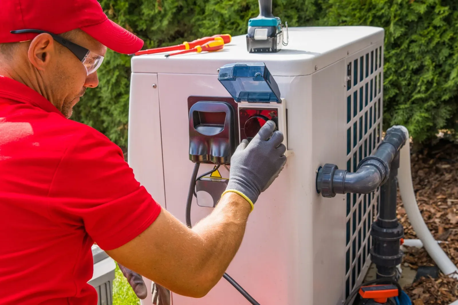 Technician servicing outdoor air conditioning unit with tools and protective gear.
