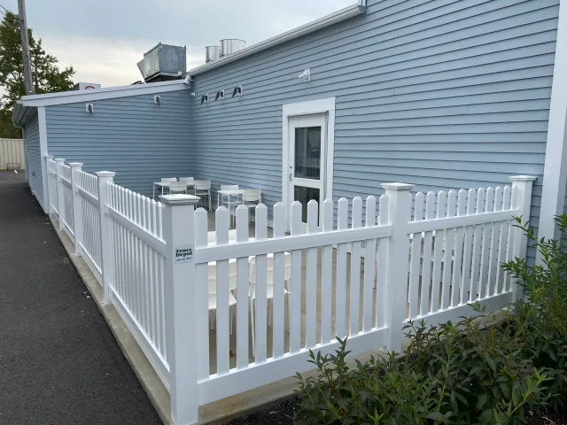 A white picket fence surrounds a patio area in front of a building.