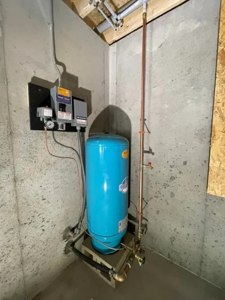 A blue water tank is sitting in a basement next to a copper pipe.