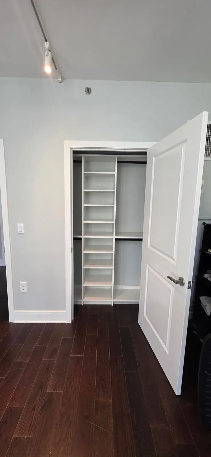 Walk-in closet with white doors and built-in shelves; dark wood floor, light gray walls.