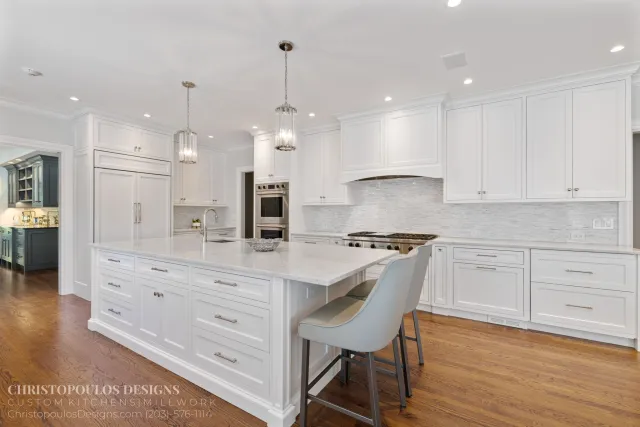 Modern white kitchen with island, stainless steel appliances, pendant lighting, and wooden flooring.