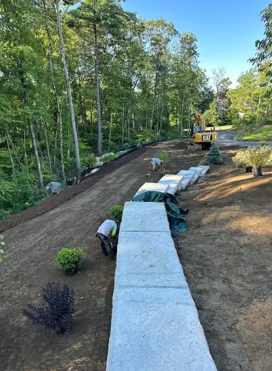 Landscaped garden path with white retaining blocks, newly graded soil, and trees along the left side