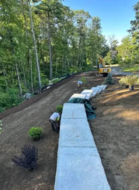 Landscaped garden path with white retaining blocks, newly graded soil, and trees along the left side