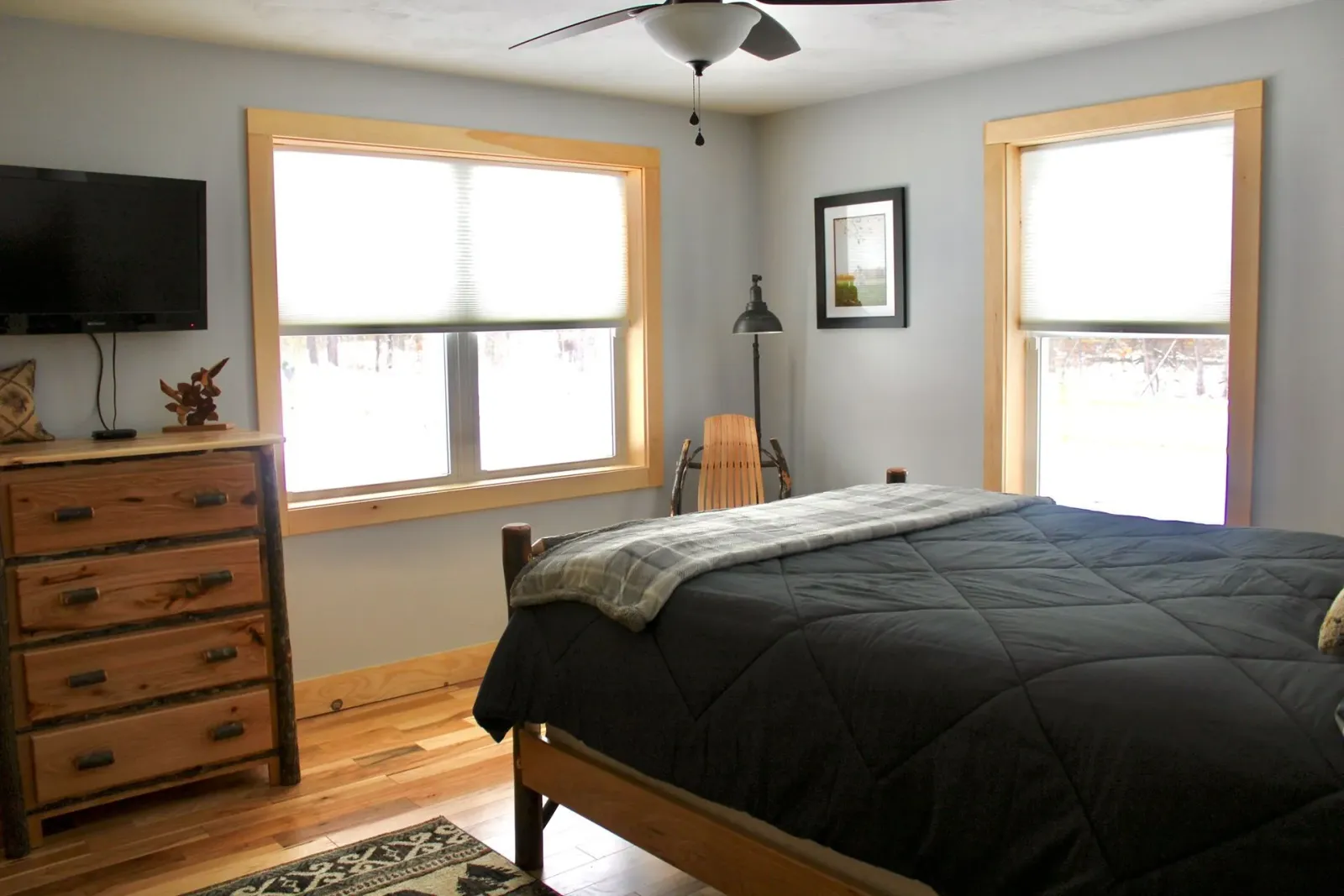 A bedroom with a bed , dresser , television and a ceiling fan.