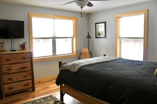 A bedroom with a bed , dresser , television and a ceiling fan.