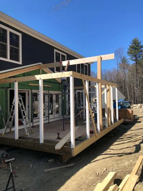 Crew member up on the framing, setting porch roof rafters on a navy two-story home
