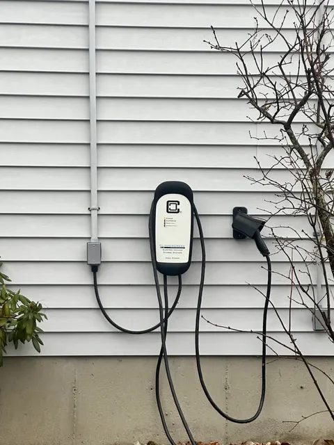A Level 2 charging station set at reach height beside the driveway with the cord holster mounted alongside.