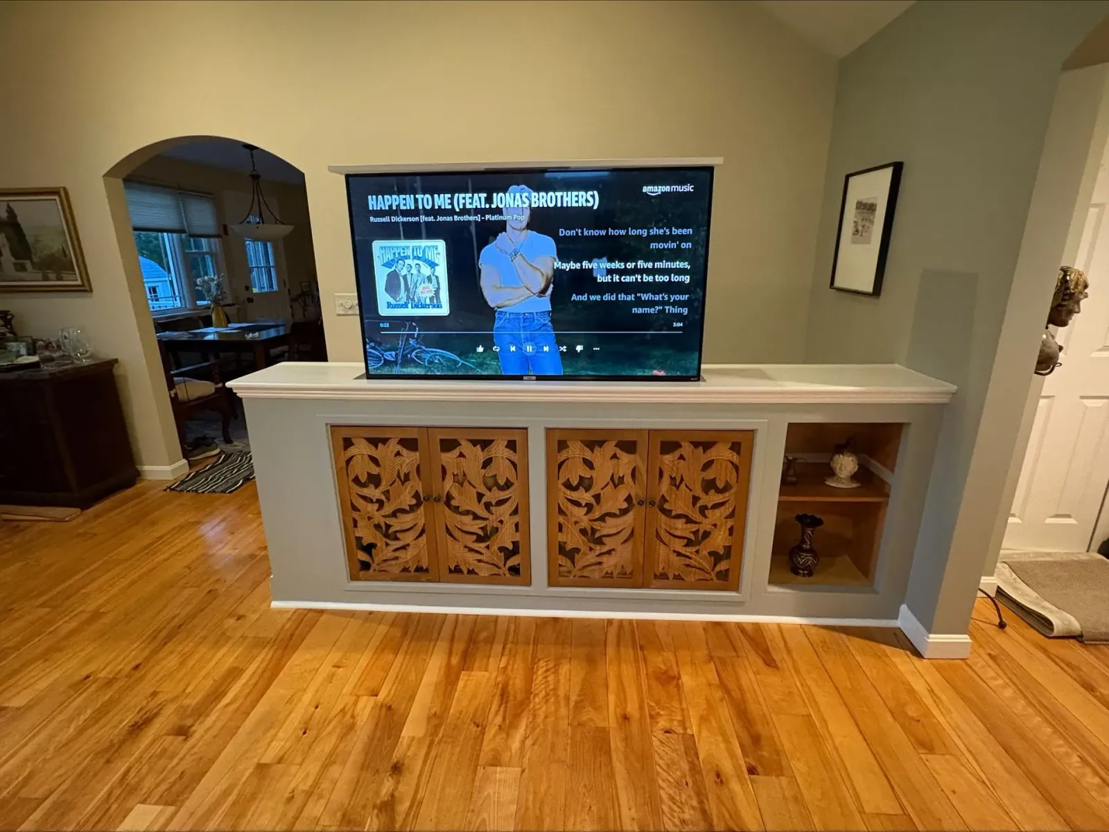 Living room with hardwood floors, a TV on a white console, and decorative carved cabinet panels.