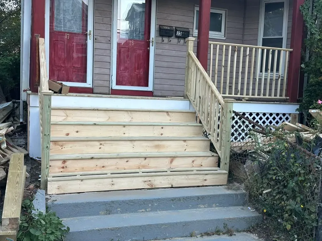 Front porch with red doors, new wooden steps, and a light wood railing beside a house