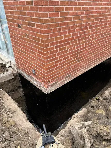 A section of a brick building foundation excavated and coated with a black waterproof sealant.